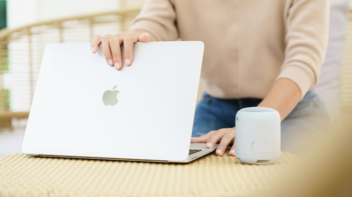 Persona con MacBook y Homepod en una mesa de mimbre.