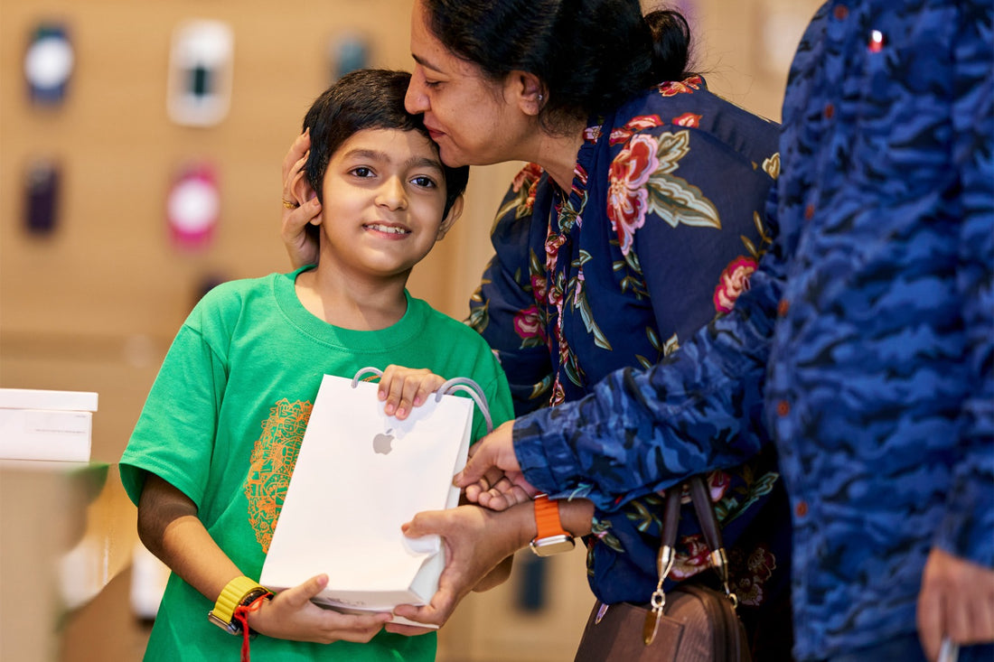 Clientes en Apple BKC Mumbai con sus compras, incluyendo el iPhone 16, ideal para capturar fotos navideñas familiares.