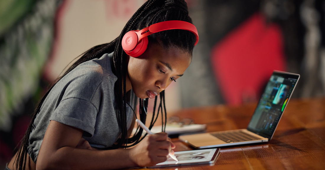 Una estudiante usa AirPods Max, mientras dibuja con un Apple Pencil en su iPad con una MacBook al frente