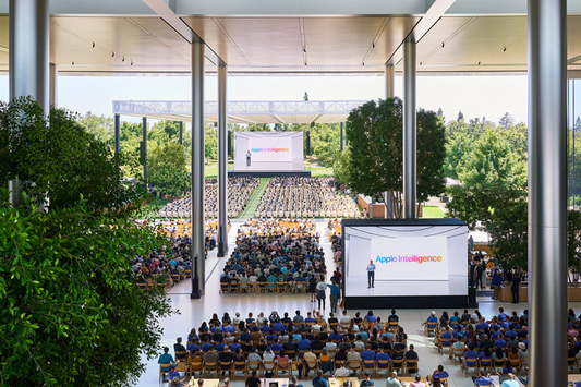 Foto que muestra a desarrolladores la presentación en grandes pantallas en el Caffè Macs del Apple Park. 